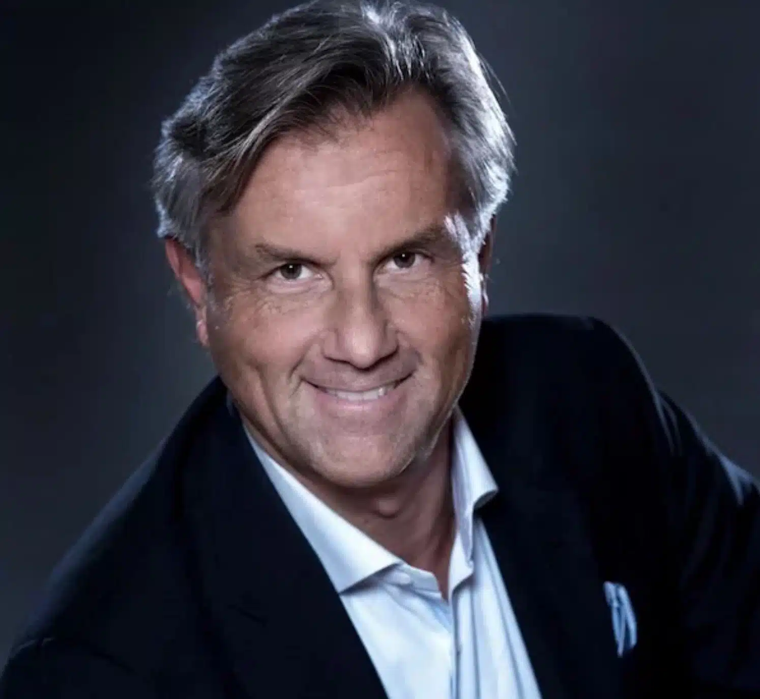 Thomas Gloor im Anzug mit grauen Haaren lächelt vor dunklem Hintergrund.