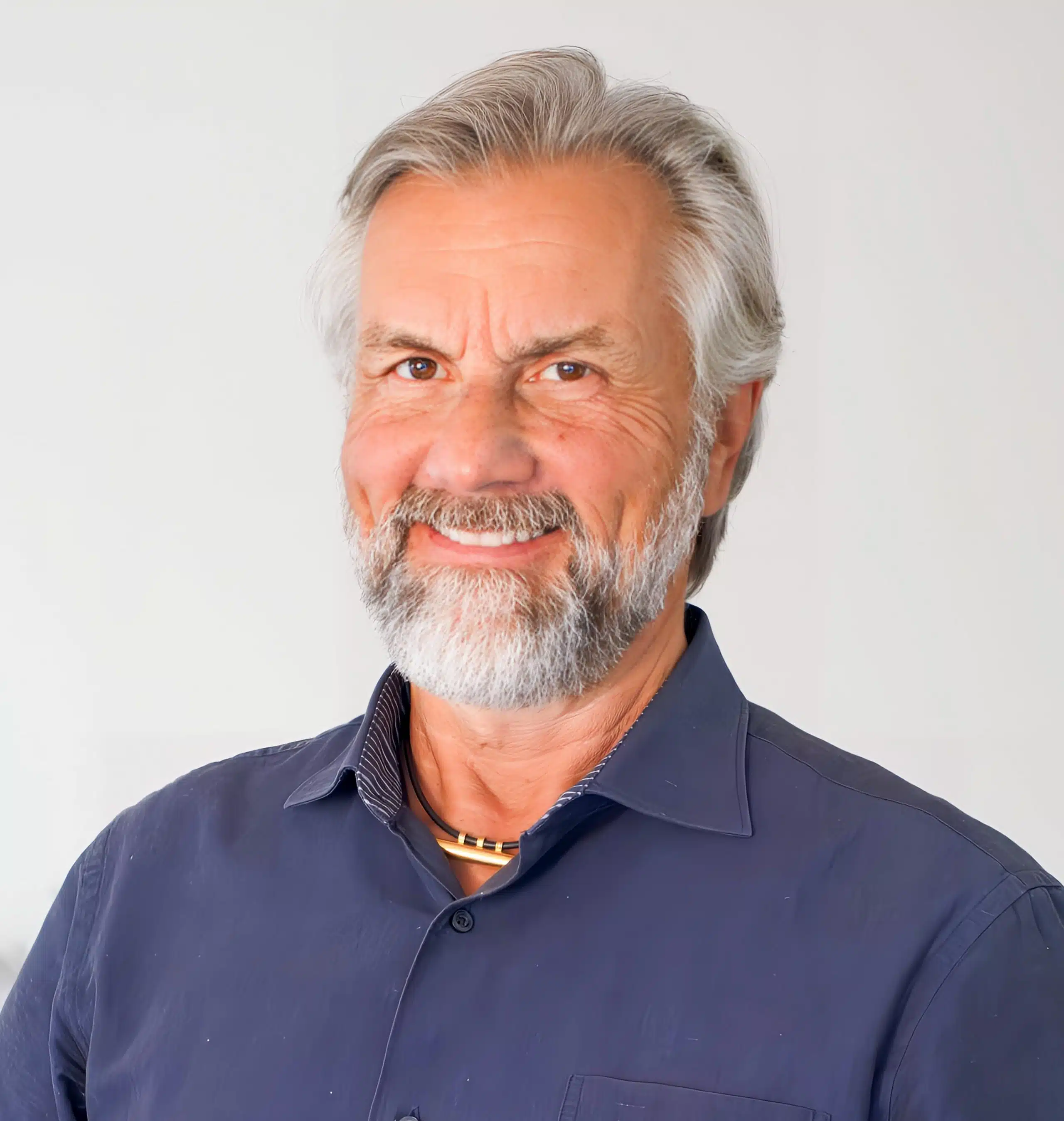 Thomas Gloor, Experte für mentale Gesundheit, mit grauem Bart und freundlichem Ausdruck steht vor hellem Hintergrund und lächelt.