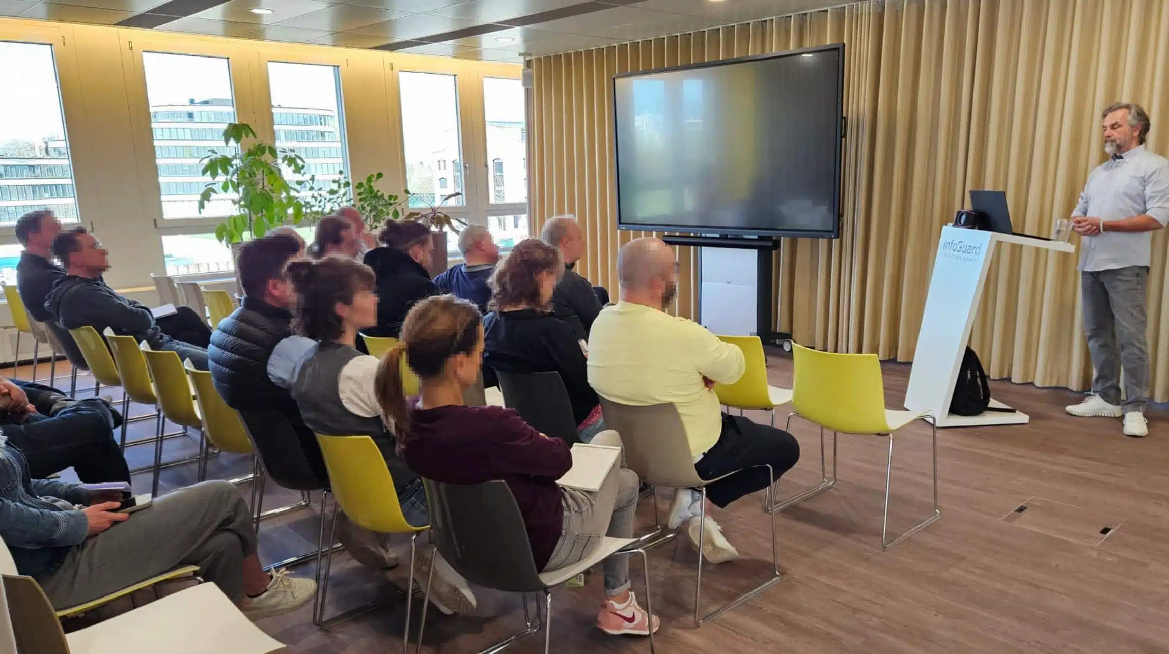 Infoguard Angestellte hören sich einen Vortrag an von Thomas Gloor. Er steht am Pult vor Bildschirm und Flipchart.