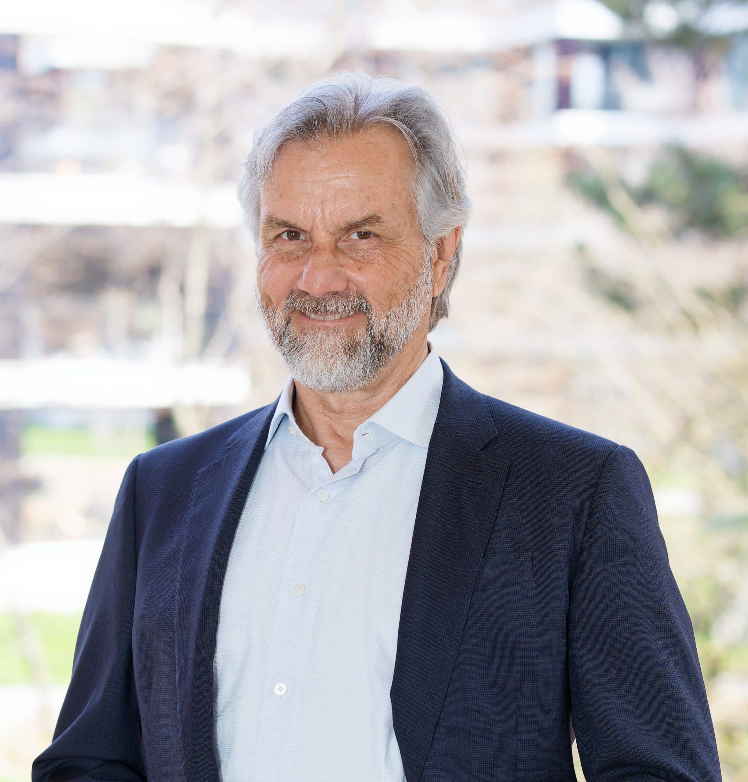 Thomas Gloor, Experte für mentale Gesundheit, mit grauem Bart und freundlichem Ausdruck steht vor hellem Hintergrund und lächelt.